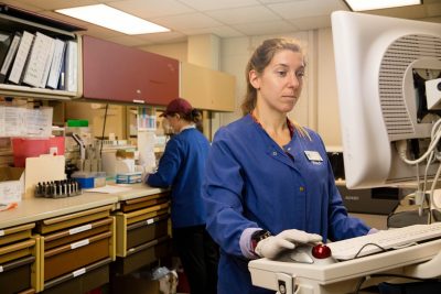 Two people wearing blue scrubs working in a lab.