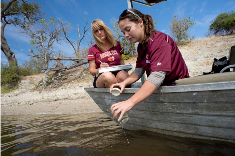 Kathleen Alexander in Botswana collecting data samples from a river while on a small boat with a student.